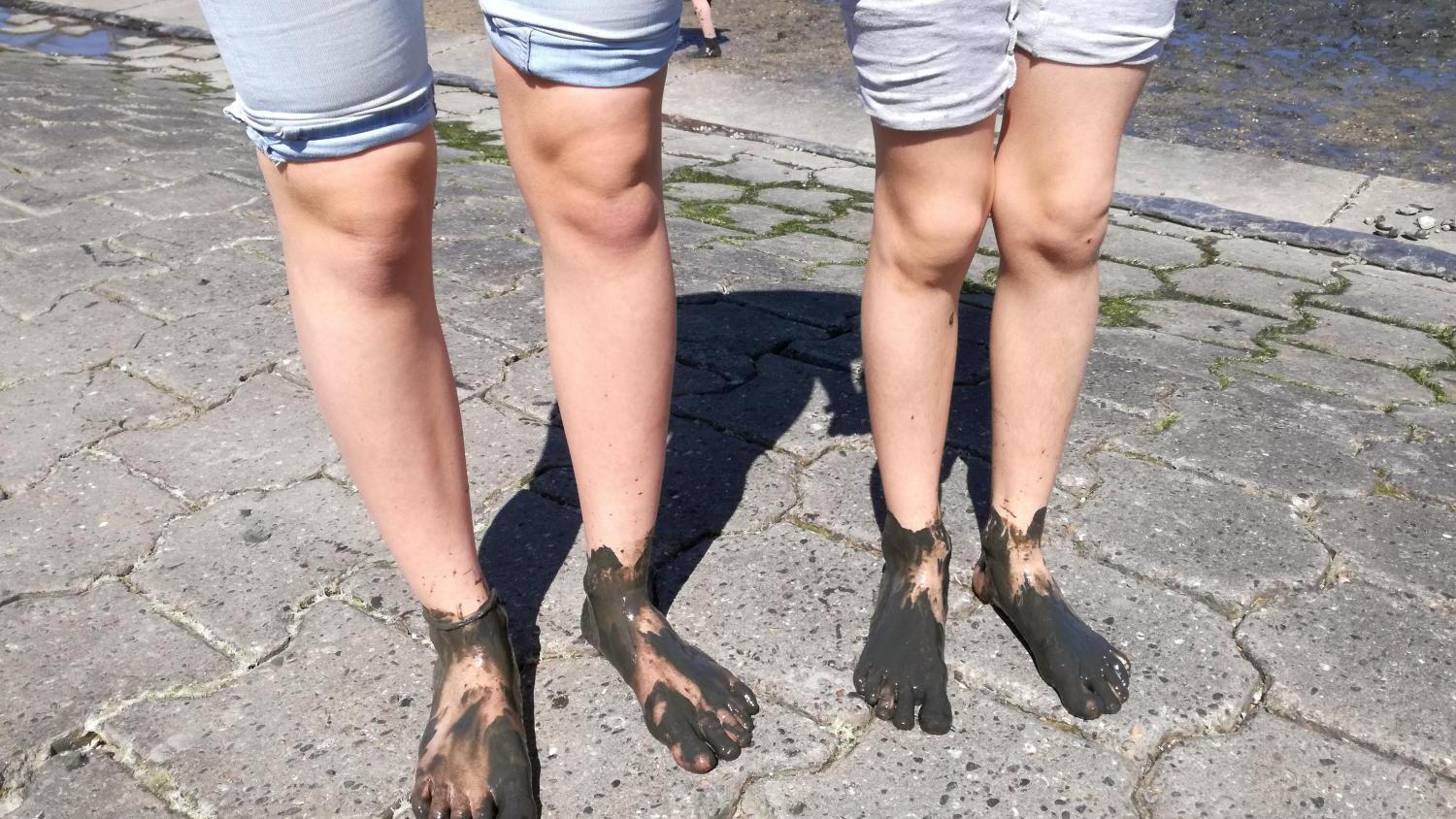 Zwei Personen mit schlammigen Füßen stehen barfuß auf Pflastersteinen.