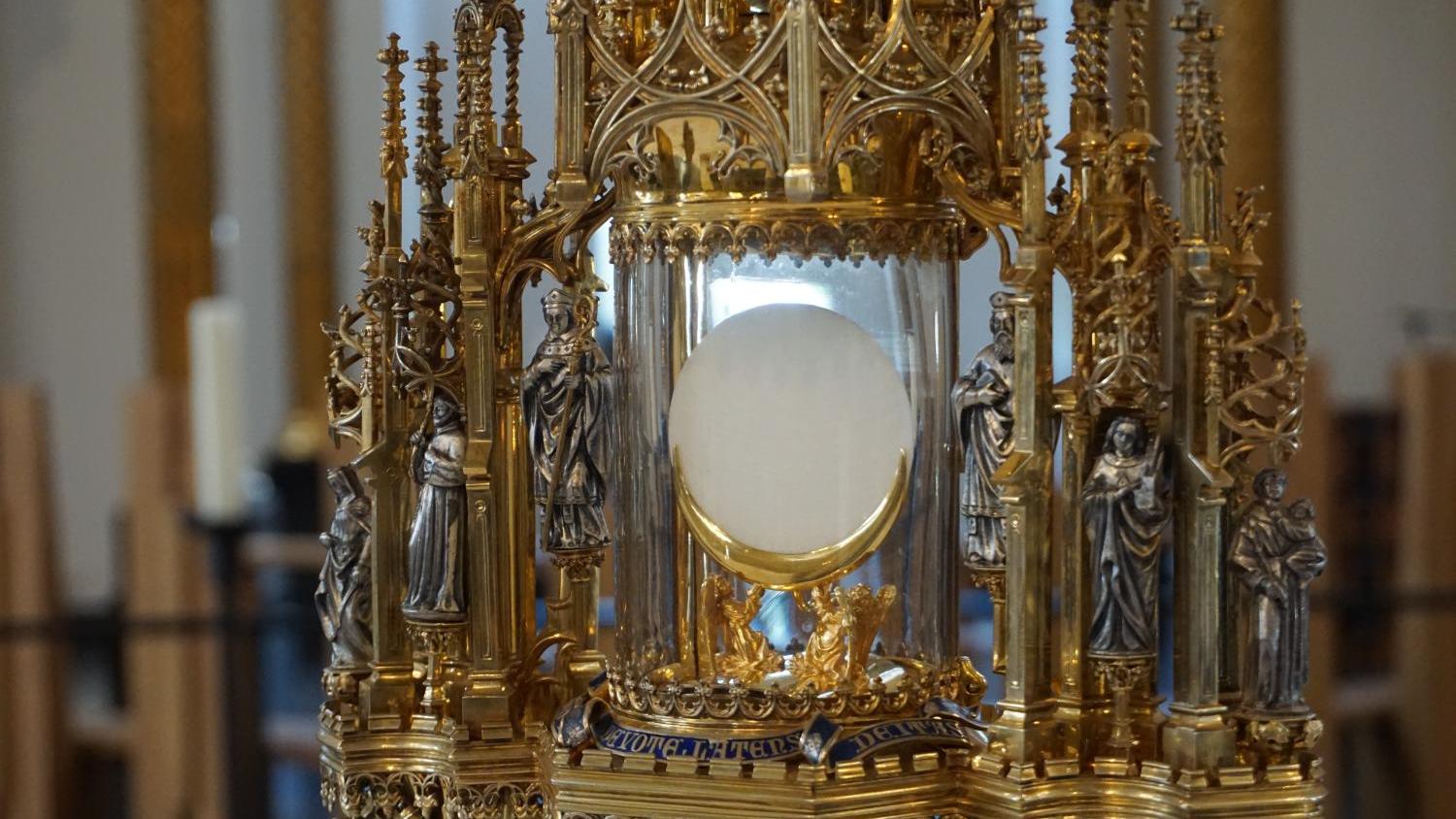 Vergoldete Monstranz mit Hostie, umgeben von Heiligenfiguren in einer Kirche.
